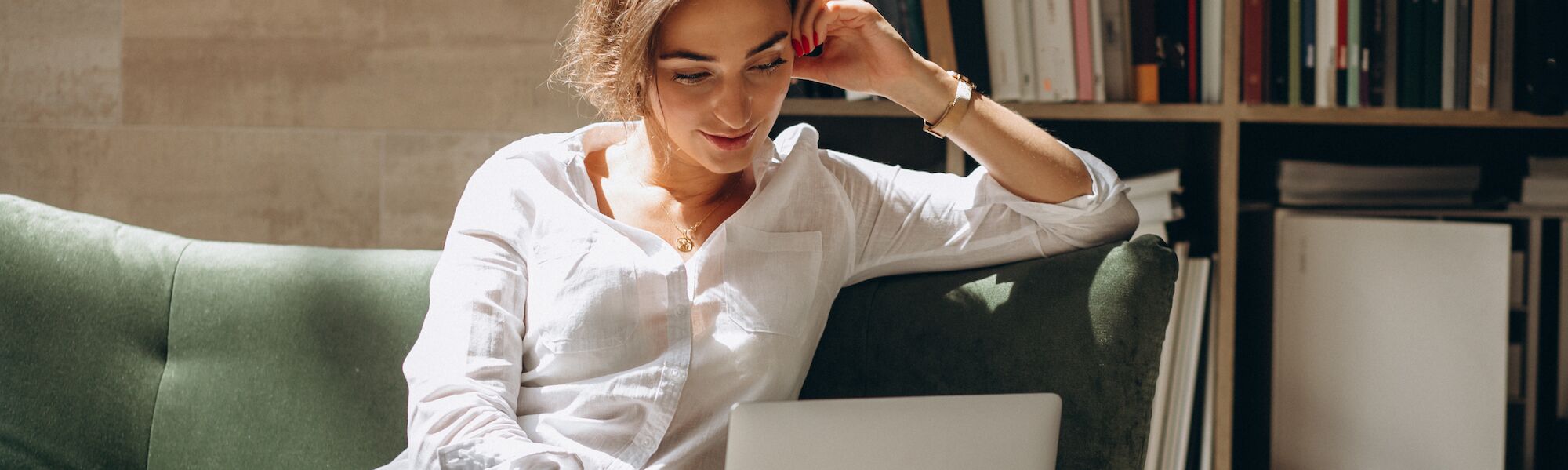 Professional woman smiling while working on laptop in modern office with bookshelves